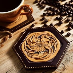 May include: Hexagonal leather coaster with a floral design. The coaster features a light brown floral pattern on a dark brown background, with white stitching around the edges. A coffee cup and coffee beans are in the background.
