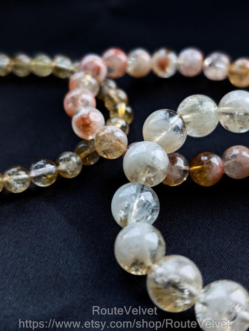 Op de afbeelding: Close-up van verschillende strengen edelsteen kralenarmbanden. De kralen zijn voornamelijk helder, met variaties van geel, oranje en bruin. De kralen zijn rond en lijken aan elkaar geregen te zijn. De achtergrond is effen zwart.