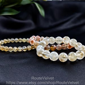 Op de afbeelding: Drie armbanden met kralen in verschillende tinten geel, oranje en transparant. De armbanden worden gepresenteerd op een zwarte satijnen ondergrond. De kralen zijn rond en lijken van gepolijste steen te zijn.