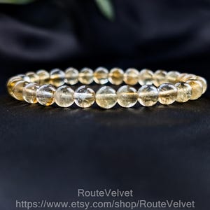 Op de afbeelding: Een armband gemaakt van ronde, doorschijnende, goudgele citrien kralen. De kralen zijn aan elkaar geregen en vormen een complete cirkel. De armband wordt gepresenteerd tegen een donkere achtergrond, die de kleur en textuur van de stenen benadrukt.