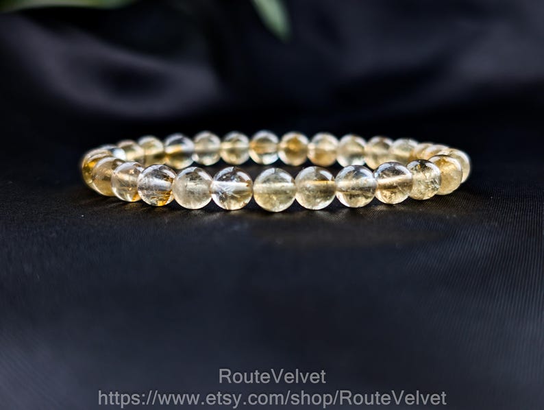Op de afbeelding: Een armband gemaakt van ronde, doorschijnende, goudgele citrien kralen. De kralen zijn aan elkaar geregen en vormen een complete cirkel. De armband wordt gepresenteerd tegen een donkere achtergrond, die de kleur en textuur van de stenen benadrukt.