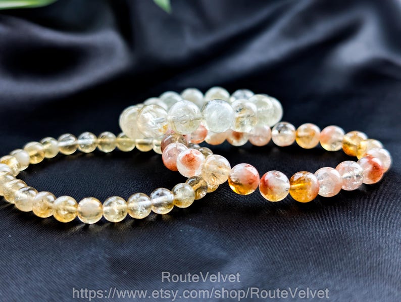 Op de afbeelding: Drie armbanden met kralen in verschillende kleuren, waaronder geel, oranje en transparant. De armbanden zijn gemaakt van ronde, gepolijste kralen. De armbanden worden op een zwart oppervlak gepresenteerd.