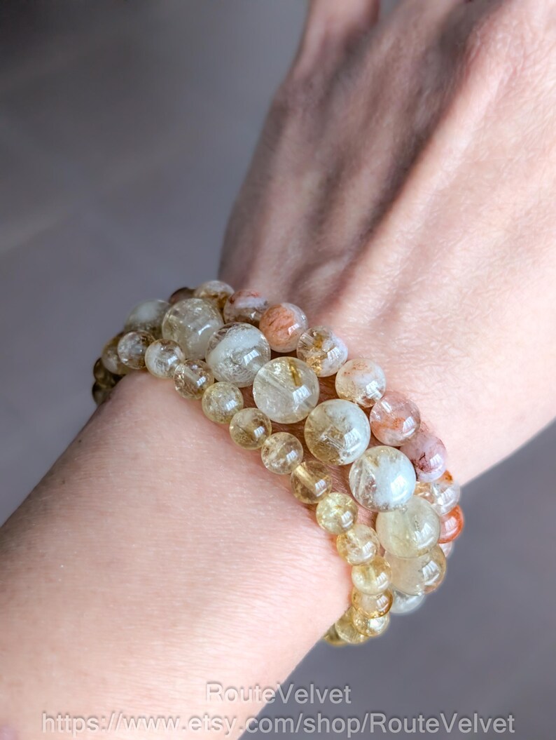 Op de afbeelding: Drie armbanden met heldere, gele en oranje gekleurde edelstenen. De armbanden zijn op een pols gestapeld, waarbij de verschillende maten van de kralen te zien zijn. De kralen zijn doorschijnend, wat een natuurlijke en aardse uitstraling geeft.