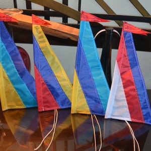 May include: Four colorful triangular flags with white stitching and strings. The flags are made of fabric and have stripes of red, blue, yellow, and white.