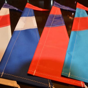 Puede incluir: Cuatro banderines triangulares de tela con costuras blancas. Los banderines son rojo, blanco y azul, azul y blanco, rojo y azul, y azul.