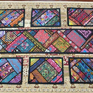 May include: A vibrant patchwork table runner with matching placemats. The runner and placemats showcase diverse fabric patterns in red, blue, green, and yellow, framed by black borders. The set is presented on a patterned rug.