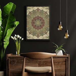 May include: A framed mandala art print with a black frame. The mandala features a detailed design in shades of green, brown, and beige. The artwork is displayed on a dark wall, with a wooden cabinet and chair in the foreground.
