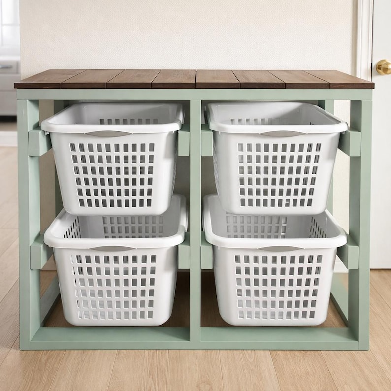 May include: A four-compartment storage unit with four white plastic laundry baskets. The unit has a light green frame and a dark brown wooden top. The baskets are rectangular with a grid pattern and gray handles.
