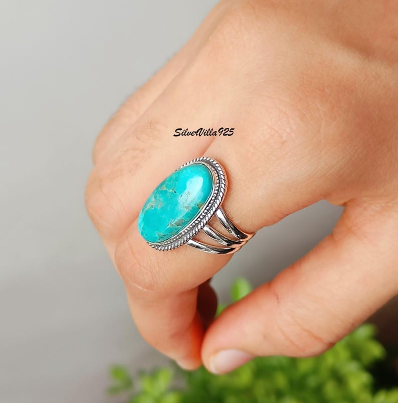 May include: A sterling silver ring featuring a large, oval turquoise stone. The stone is a vibrant turquoise color, set in a rope-style bezel. The ring has a triple-band design. The text "SilverVilla925" is visible.