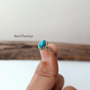 Może przedstawiać: Srebrny pierścionek z turkusowym kamieniem w kształcie łzy. Pierścionek ma obramowanie z koralików wokół kamienia i teksturowaną obręcz. Pierścionek jest trzymany przez palce osoby. Tekst "BaniThani92" jest na zdjęciu.