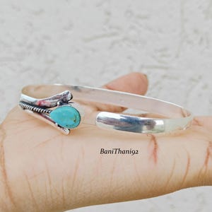 May include: A silver cuff bracelet featuring a turquoise gemstone. The bracelet has an open design with a decorative section near the stone. The turquoise stone is a bright blue-green colour. The bracelet is open, allowing for easy wear.