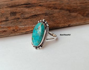 May include: A silver ring featuring a large, oval turquoise stone. The stone is a vibrant teal color with natural variations. The ring has a detailed, beaded border and a split shank design. The text "BaniThani92" is visible on the right side.