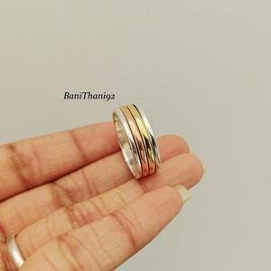 May include: A silver ring with three bands in rose gold, gold, and silver. The ring is held in a hand against a light background. The text "BaniThani92" is in the upper left corner.