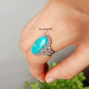 May include: A sterling silver ring featuring a large, oval turquoise stone. The stone is a vibrant turquoise color, set in a rope-style bezel. The ring has a triple-band design. The text "SilverVilla925" is visible.
