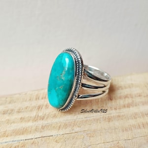 May include: A silver ring featuring a large, oval turquoise stone. The stone is a vibrant teal color with natural matrix patterns. The ring has a textured border around the stone and a triple-band design. The text "SilverVilla925" is visible on the ring.