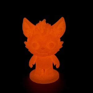 Könnte beinhalten: Orange leuchtende Figur eines Cartoon-Fuchses mit großen Ohren, stehend auf einem kreisförmigen Sockel. Der Fuchs hat einen freundlichen Ausdruck und wird vor einem schwarzen Hintergrund beleuchtet. Die Figur ist etwa 7.6 cm groß.