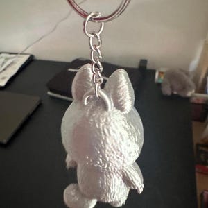 May include: A silver-colored bunny keychain with a textured surface. The bunny is attached to a silver chain and keyring. The keychain is a cute accessory.