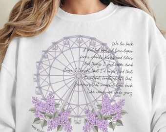 May include: White sweatshirt with a Ferris wheel design, purple floral accents, and the text "We lie back...THE ELDEST DAUGHTER." The design includes a poem. A comfortable, casual garment.