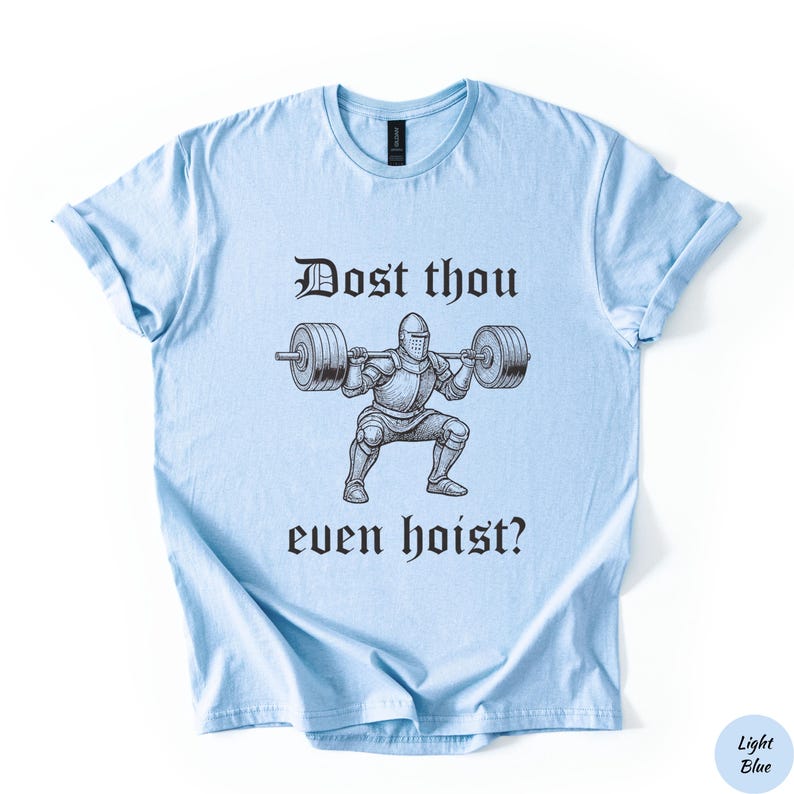 Op de afbeelding: Lichtblauw T-shirt met de tekst "Dost thou even hoist?" boven en onder een zwart-wit illustratie van een ridder die gewichten heft. Het shirt heeft een lichtblauwe kleur.