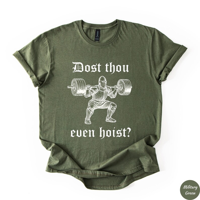 Op de afbeelding: Militairgroen t-shirt met opgerolde mouwen. Het shirt heeft een witte afbeelding van een ridder die gewichten heft, met de tekst "Dost thou even hoist?" in een middeleeuws lettertype. Het shirt is gemaakt van zacht materiaal.