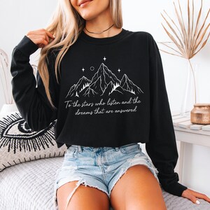 Puede incluir: Sudadera negra de manga larga con un dise&ntilde;o de monta&ntilde;a blanco y el texto "To the stars who listen and the dreams that are answered." La sudadera est&aacute; hecha de un material suave.