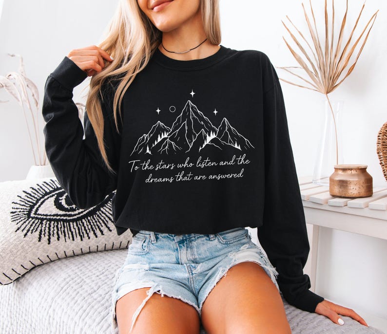 Puede incluir: Sudadera negra de manga larga con un dise&ntilde;o de monta&ntilde;a blanco y el texto "To the stars who listen and the dreams that are answered." La sudadera est&aacute; hecha de un material suave.