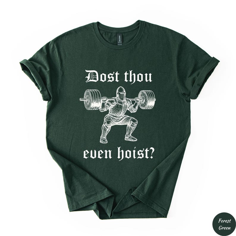Op de afbeelding: Bosgroen t-shirt met een witte afbeelding van een ridder die een halter heft. De tekst "Dost thou even hoist?" staat boven en onder de illustratie. Het shirt is gemaakt van zacht materiaal.