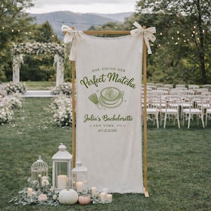 Könnte beinhalten: Ein cremefarbenes Banner mit dem Text "She found her Perfect Matcha" und "Julia's Bachelorette, New York, NY, 20.12.2026" in Grün. Das Banner wird auf einem Holzrahmen mit weißen Schleifen präsentiert.