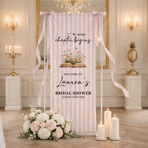 Könnte beinhalten: Ein rosa-weiß gestreiftes Banner für eine Brautparty mit dem Text "a new chapter begins" und "Welcome to Lauren's". Das Banner zeigt eine Illustration eines offenen Buches mit Blumen und Schmetterlingen. Das Datum der Party ist der 24. August 2026.