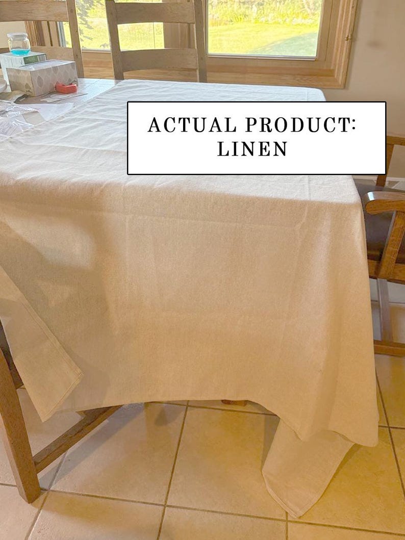 Pu&ograve; includere: Una tovaglia di lino bianca drappeggiata su un tavolo di legno. Il testo "ACTUAL PRODUCT: LINEN" &egrave; visualizzato in un rettangolo bianco. Sedie di legno circondano il tavolo, con una finestra visibile sullo sfondo. La tovaglia &egrave; di lino.