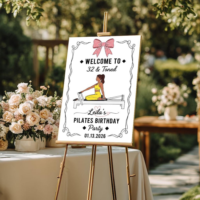 May include: A white sign on a gold easel with the text "WELCOME TO 32 & Toned" and "Leila's PILATES BIRTHDAY Party 01.13.2026". The sign features a pink bow and an illustration of a person doing Pilates.