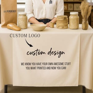 May include: A table setting with a beige tablecloth featuring a custom design. The table displays various items, including jars, a bowl, wooden objects, and a paper bag with the text "AA PONDERLY". The text "CUSTOM LOGO" and "custom design" are also visible.
