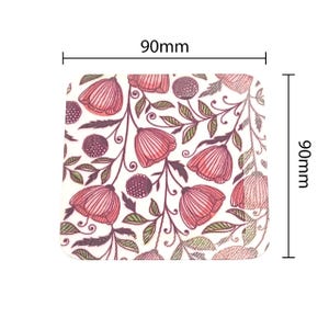 Puede incluir: Posavasos cuadrado de 90mm x 90mm con diseño floral. Presenta flores rosas, hojas verdes y bayas moradas oscuras sobre fondo blanco. El patrón floral se repite en toda la superficie.