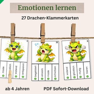 Może przedstawiać: Karty edukacyjne do nauki emocji, z kreskówkowymi smokami. Karty są przypięte do sznurka drewnianymi spinaczami. Tekst na kartach zawiera "Ucz się emocji" i "27 kart zaciskowych Smoka".