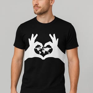 May include: Black t-shirt featuring a white graphic of hands forming a heart shape, with a world map in the center. The shirt is a classic crew neck style, made of a soft material. The design is simple and eye-catching.