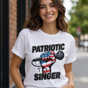 Puede incluir: Camiseta blanca con el texto "PATRIOTIC SINGER" sobre un gráfico de un puño sosteniendo un micrófono, pintado con los colores de la bandera americana. Una cruz plateada cuelga del micrófono. La modelo lleva vaqueros azules.