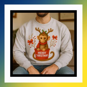 May include: A light gray sweatshirt featuring a cartoon monkey wearing a red scarf and antlers, sitting in a red cup with the words "MERRY CHRISTMAS". The design includes red bows and sprigs.