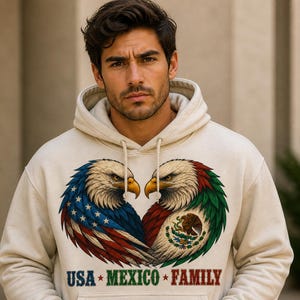 Può includere: Una felpa con cappuccio color crema con due aquile che si fronteggiano. Un'aquila ha il design della bandiera americana e l'altra il design della bandiera messicana. Il testo "USA * MEXICO * FAMILY" è stampato sotto le aquile.