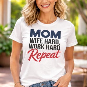 May include: White t-shirt with the text "MOM WIFE HARD, WORK HARD, Repeat" in navy blue and red lettering. The shirt is worn by a person wearing blue jeans.