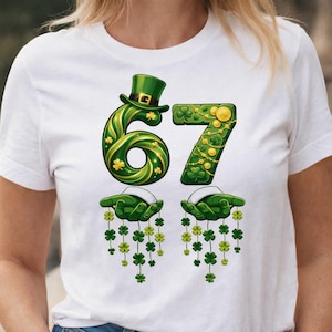May include: White t-shirt with a St. Patrick's Day graphic. The design shows the number 67 in green, adorned with shamrocks and gold coins. Below are two green hands holding shamrock garlands, a festive design.
