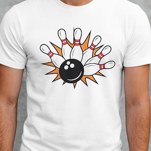 May include: White t-shirt featuring a bowling-themed graphic. The design includes a black bowling ball striking white bowling pins with red stripes, set against an orange burst. A fun, sporty design.