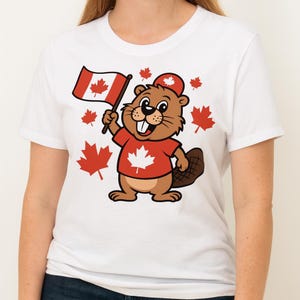 Könnte beinhalten: Weißes T-Shirt mit einem Cartoon-Biber, der ein rotes Hemd und eine rote Mütze trägt und eine kanadische Flagge hält. Rote Ahornblätter umgeben den Biber, ein patriotisches Design.