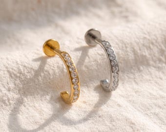 May include: Two curved labret studs featuring a row of clear, round-cut stones set along the front. One stud is finished in a polished gold tone, while the other is finished in a polished silver tone, each with a flat circular back disc.