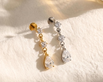May include: Two dangling body jewellery pieces, one in gold tone and one in silver tone. Each features a flat circular back, two small round clear stones, and a larger pear-shaped clear stone at the bottom, all connected by thin metal links.