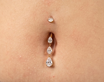 May include: A gold-toned navel ring featuring a small round clear stone at the top and a vertical drop attachment consisting of three graduated pear-shaped clear stones linked together in a descending arrangement.