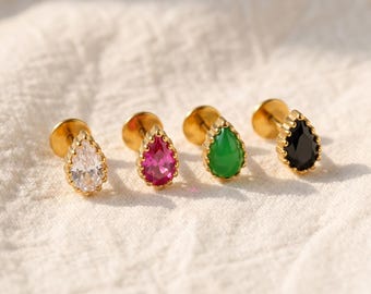 May include: Four gold-tone stud earrings featuring teardrop-shaped stones in clear, fuchsia, green, and black. Each earring has a flat circular back and a scalloped metal setting surrounding the faceted gemstone in a pear-cut design.