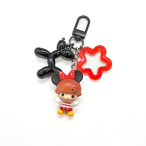 May include: A keychain featuring a cartoon character with a red bow, black ears, and a red and white striped shirt. The keychain also includes a black balloon dog charm and a red star-shaped charm. The keychain has a silver clasp.