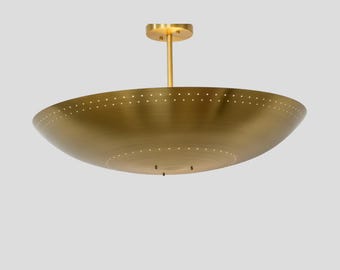 May include: A brass-colored, bowl-shaped ceiling light fixture. The fixture has a circular base and a central rod. The bowl has a series of small, evenly spaced holes around the rim. The light is suspended from the ceiling.