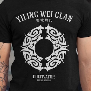 May include: Black crew neck t-shirt with white text and a circular tribal design. The text reads "YILING WEI CLAN" above the design and "CULTIVATOR BURIAL MOUNDS" below. The shirt is short-sleeved.