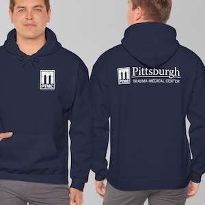 May include: Navy blue hoodie with a front pocket and hood. The front features a white square logo with the letters "PTMC". The back displays the words "Pittsburgh Trauma Medical Center" in white.